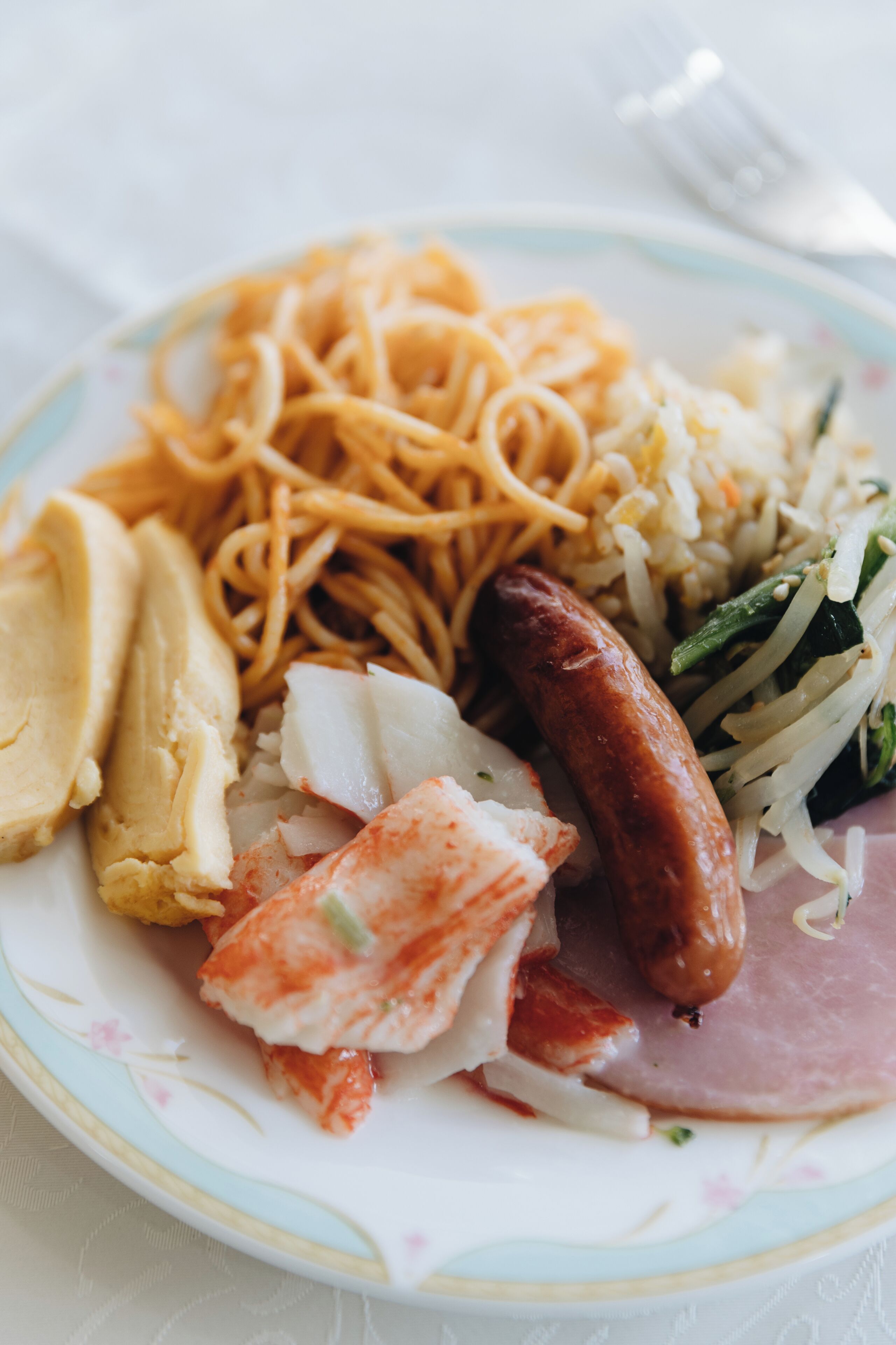 A plate with noodles, sausage, and various vegetables.
