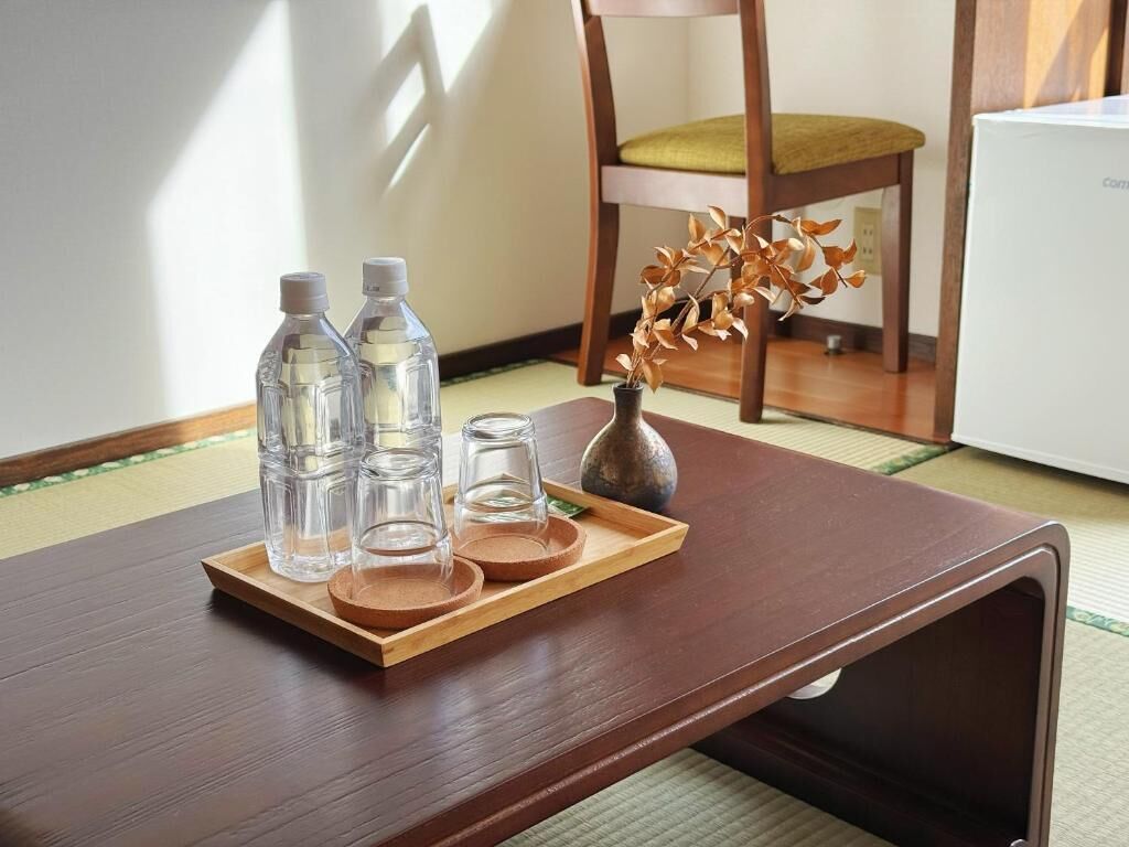 Une table en bois, avec des bouteilles transparentes et un vase contenant des feuilles séchées.