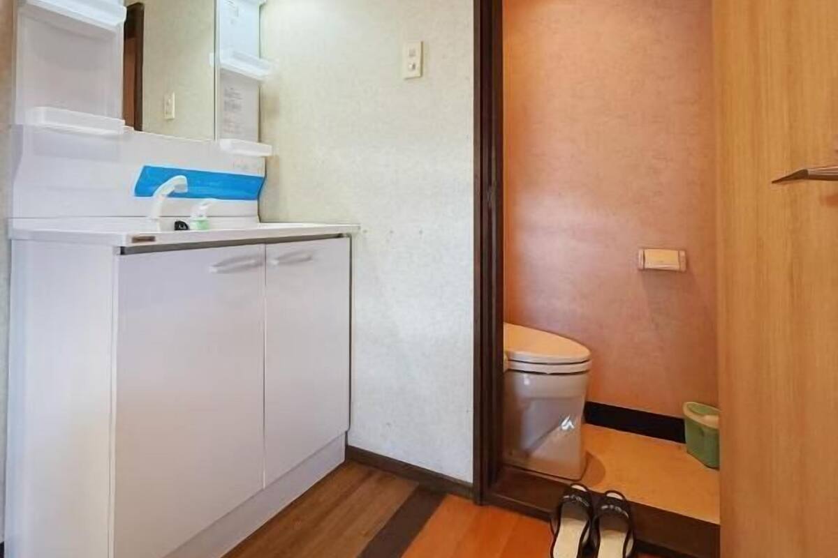 A small bathroom with a toilet, a sink with a mirror, and a pair of shoes on the floor.