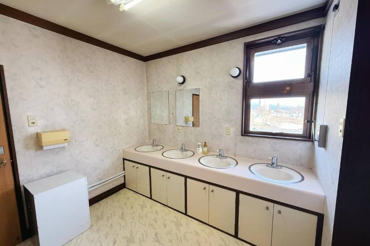 A bathroom with three sinks, a mirror, a window, and a white cabinet.
