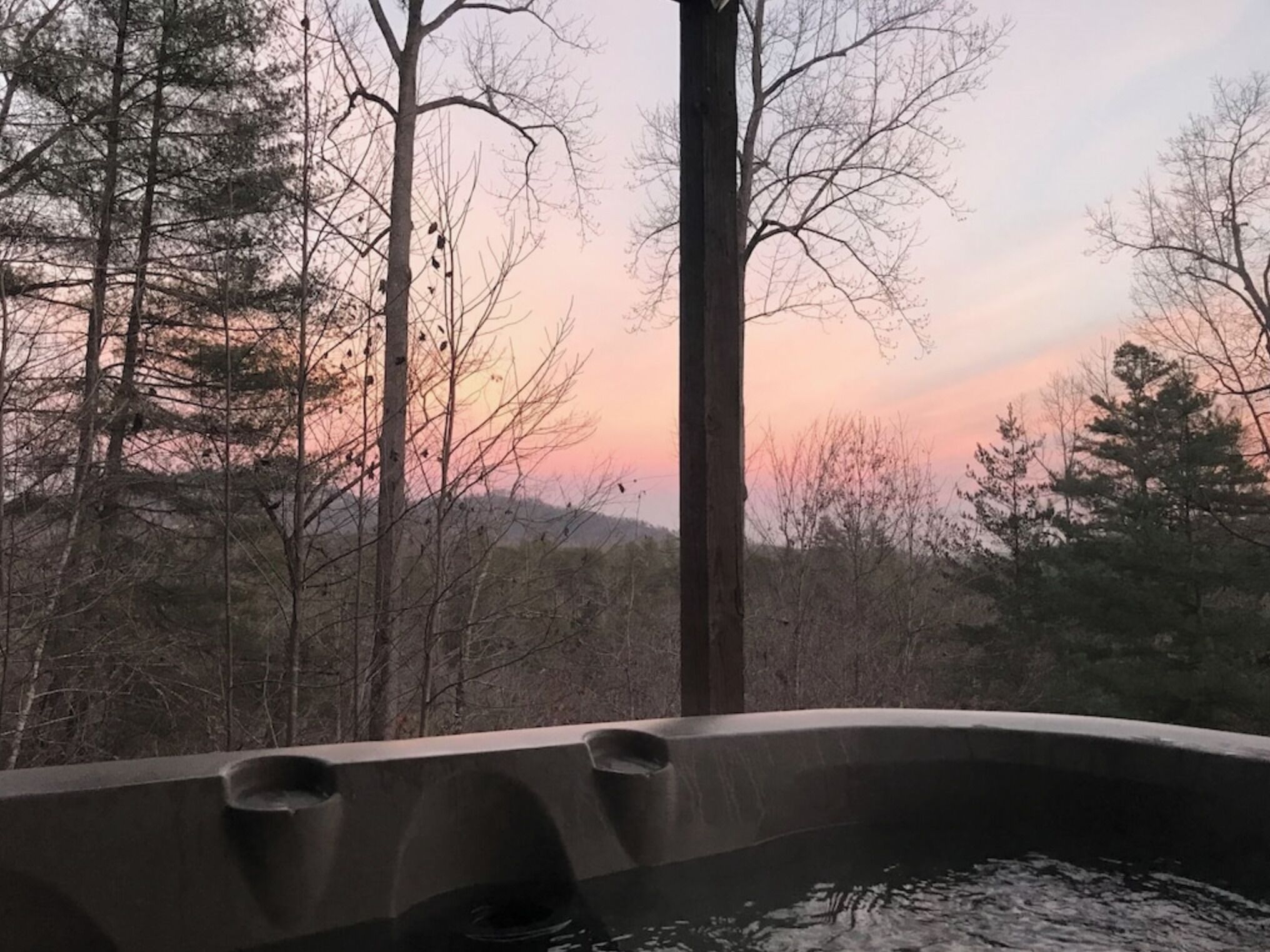 A hot tub with a view of a forest and a sunset.