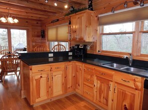 Een houten keukentje in een chalet, met een centraal eiland, houten kastjes, een zwart aanrecht en een raam.