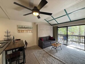 Una sala de estar moderna con comedor, ventilador de techo, ventana grande y balcón.