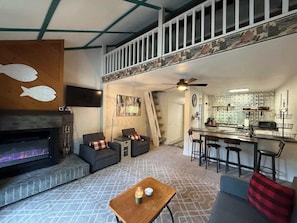 Un espacio habitable tipo loft con chimenea, sofás, comedor con taburetes de bar y cocina con salpicadero de azulejos.