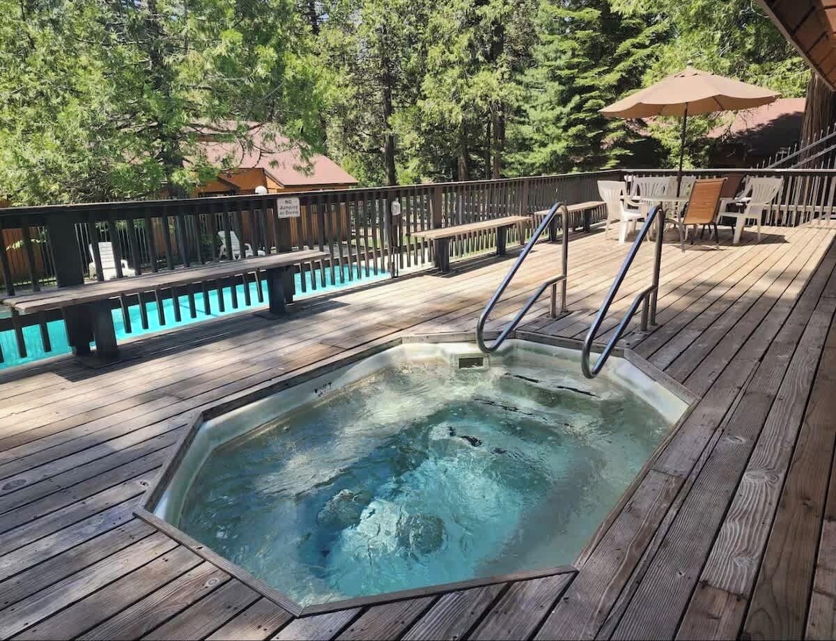 Een houten terras met een jacuzzi, buitenmeubels en uitzicht op bomen.