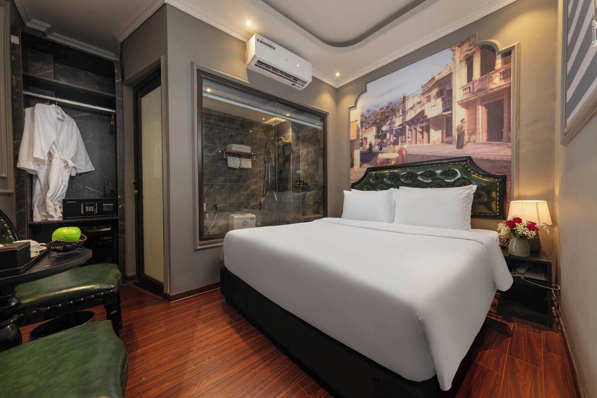 Habitación de hotel con una cama grande, ducha, escritorio con silla y un cuadro en la pared.
