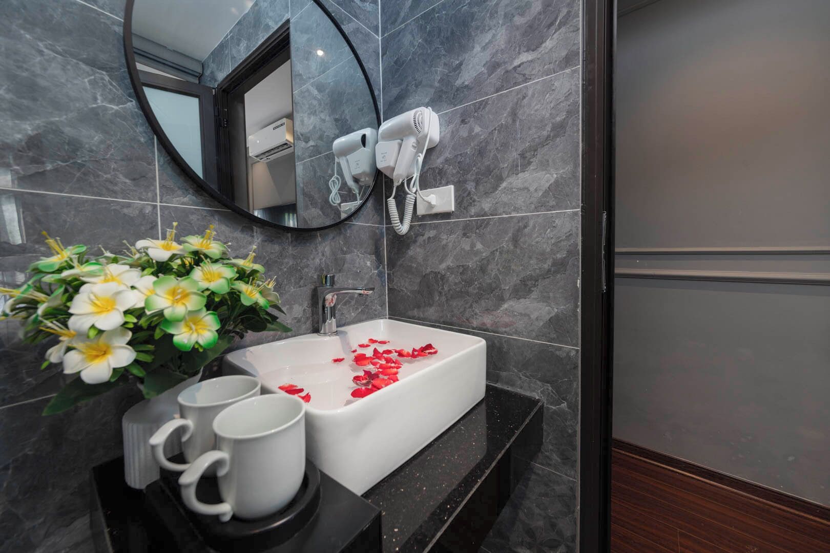A bathroom with a white sink, a mirror, and a hairdryer on the wall.