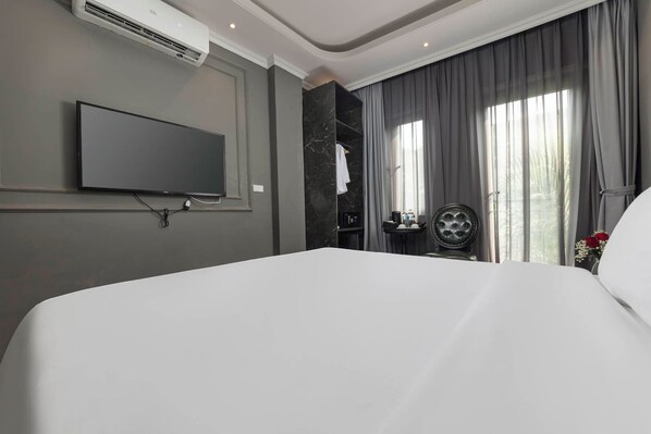 A hotel room with a large bed, a flat-screen TV mounted on the wall, a marble accent wall, a vanity with a mirror, and a window with curtains. - Hanoi Sense Legend Hotel & Travel (Hanoi)