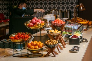 Een buffet met diverse soorten fruit en groenten, waaronder appels, tomaten en sinaasappels.