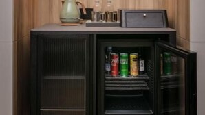 Una kitchenette compacta con un refrigerador integrado, una cafetera y una estantería con bebidas.