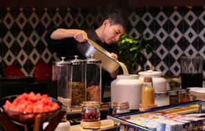 A buffet setup with various food containers and a person pouring from a jug.