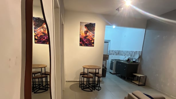 A modern living room with a sofa, a dining area with chairs, a kitchen in the background, and a large mirror on the wall. - Apartment 65m2 - comfortable, stylish, pet friendly, easy access to shops. (São Paulo)