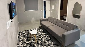 A modern living room with a grey sofa, a patterned rug, a flat-screen TV, and a door leading to another room. - Apartment 65m2 - comfortable, stylish, pet friendly, easy access to shops. (São Paulo)