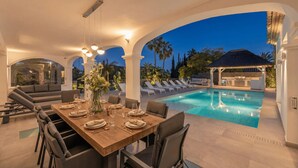 Ein Essbereich im Freien mit Pool, Liegestühlen und einer überdachten Grillanlage.