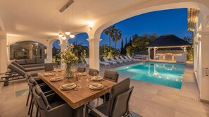 An outdoor dining area with a pool, lounge chairs, and a covered barbecue area. - Villa Promise by Vacation Marbella (Estepona)