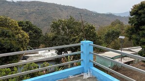 Une rambarde bleue surplombe un paysage vallonné, avec des bâtiments visibles à l’arrière-plan.
