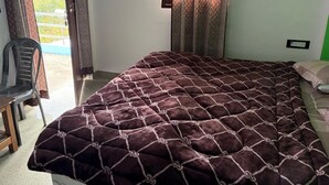 Une pièce comprenant un lit, une chaise, une fenêtre avec des rideaux et donnant sur l’extérieur.