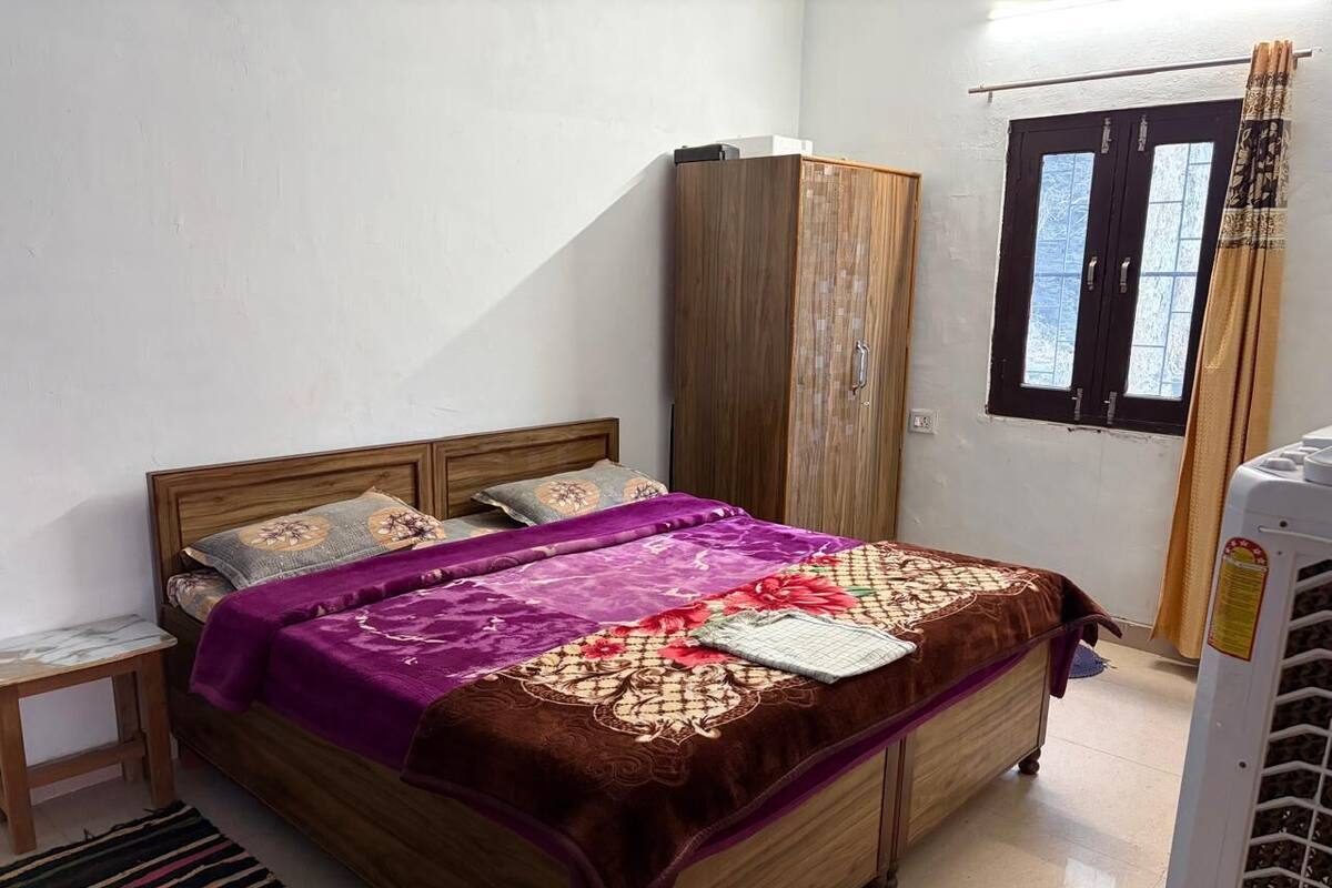 A bedroom with a bed, wooden wardrobe, and a window with curtains.