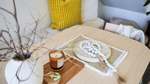 A room with a wooden table, a candle, a decorative plate, and a vase with branches. - Water’s Edge: 4BR all-ensuite. Sweeping estuary views for families and groups. (Falcon)