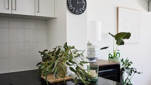 A kitchen with white cabinets, a black clock, a glass candle holder, and a potted plant. - Water’s Edge: 4BR all-ensuite. Sweeping estuary views for families and groups. (Falcon)