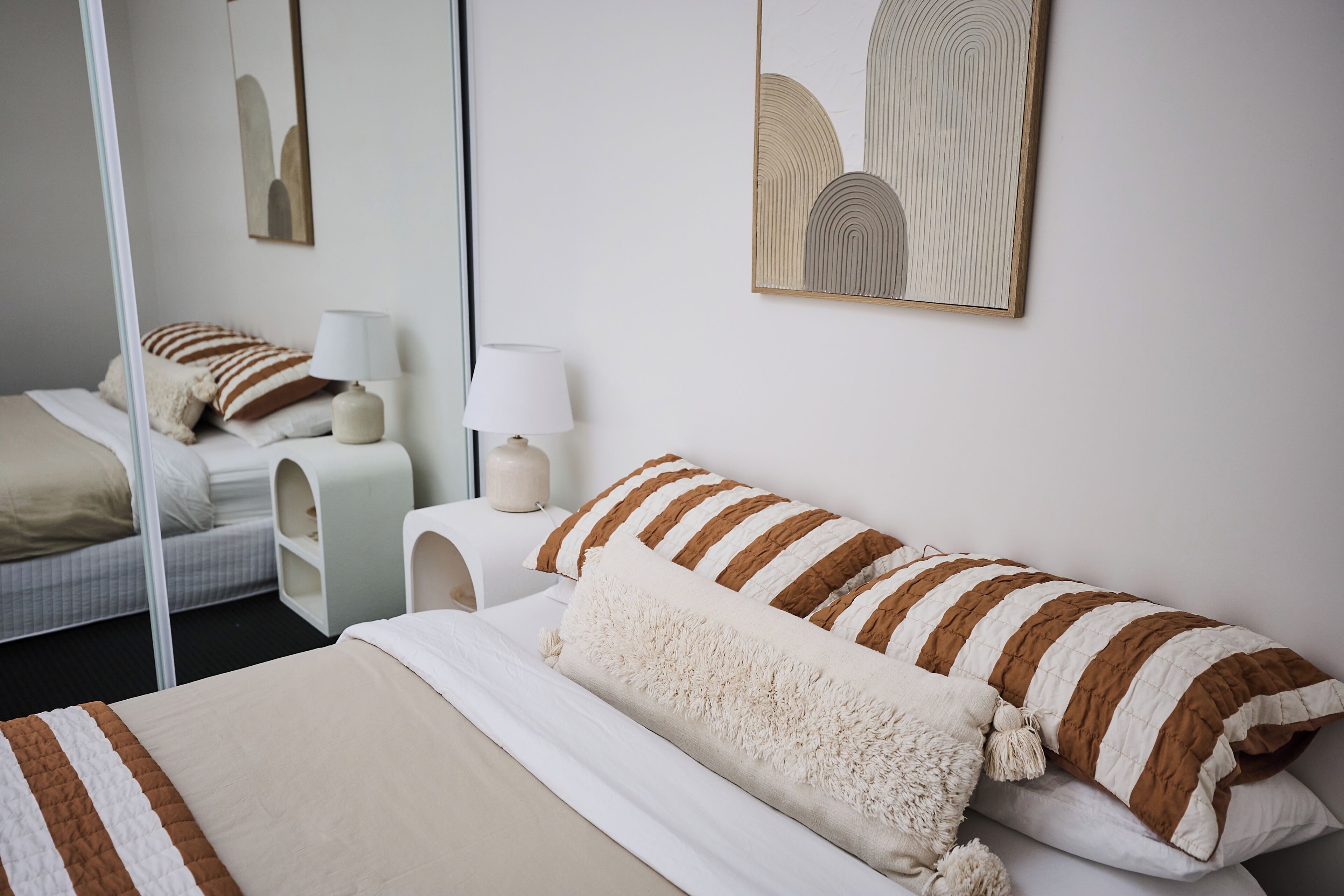 Ein Hotelzimmer mit Bett, Nachttischen, einer Lampe und Kunstwerken an den Wänden.