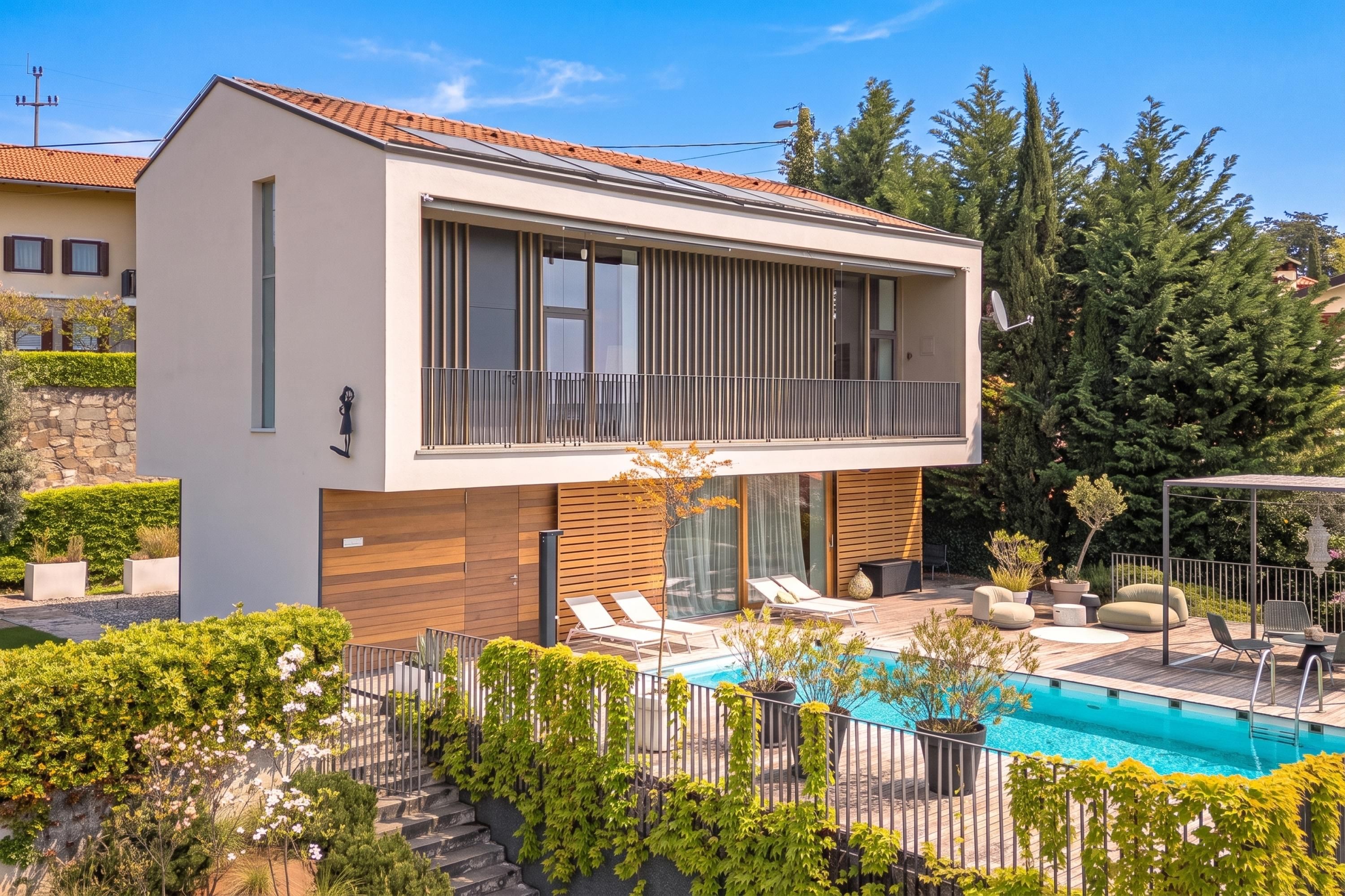 A modern two-story house with a balcony, a swimming pool, and a well-maintained garden.