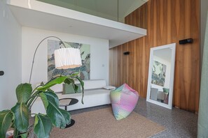 Un interior moderno con un sofá blanco, un sillón orejero de colores, un espejo grande y una planta.
