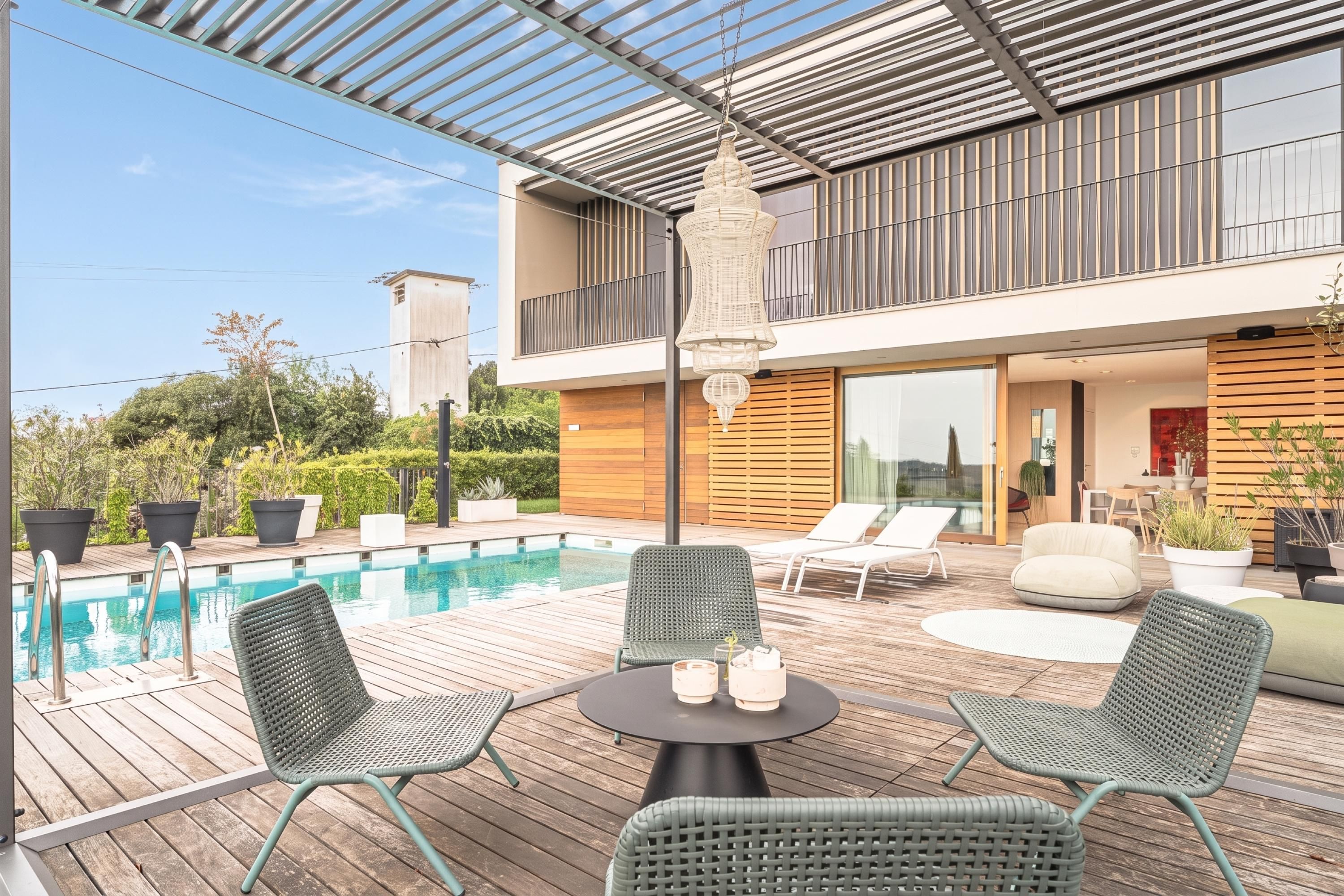 Ein moderner Poolbereich im Freien mit Liegestühlen und einem Tisch, umgeben von einer Holzterrasse.