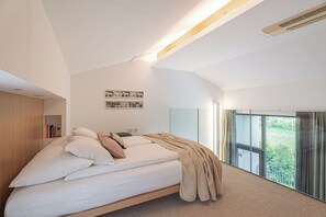 Ein modernes Schlafzimmer mit Bett, Bücherregal, Wandbild und großem Fenster mit Blick.