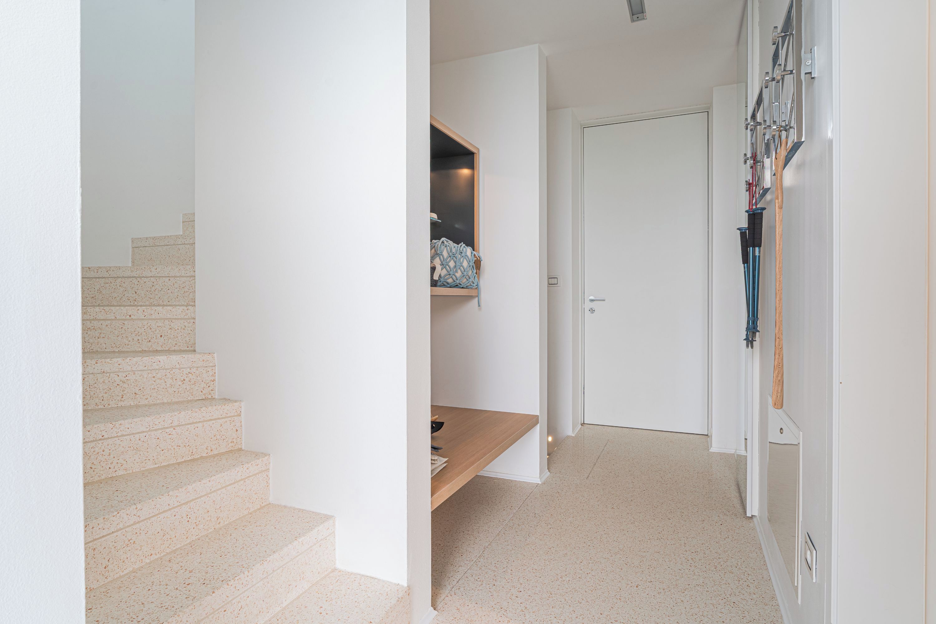 Un escalier menant à un palier où se trouvent une étagère et une porte.