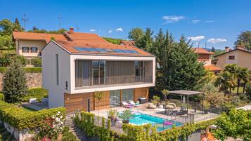 Una casa moderna de dos pisos con piscina, paneles solares y un jardín bien cuidado.