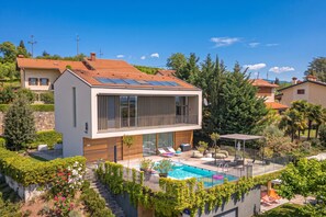 Et moderne hus i to etager med swimmingpool, solpaneler og en velplejet have.