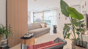 A modern living room with a sofa, a round coffee table, and a wicker chair. There are large green plants and a wooden column. - Alma Vista Villa in Goriska Brda Pool & Spa (Brda)