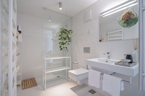 Ein modernes Badezimmer mit einer Duschkabine aus Glas, einem weißen Waschbecken und einem großen Spiegel.