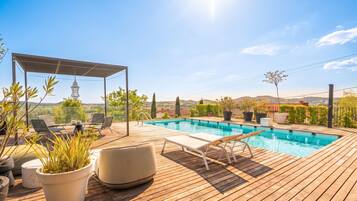 A wooden deck with a swimming pool, lounge chairs, and a pergola.
