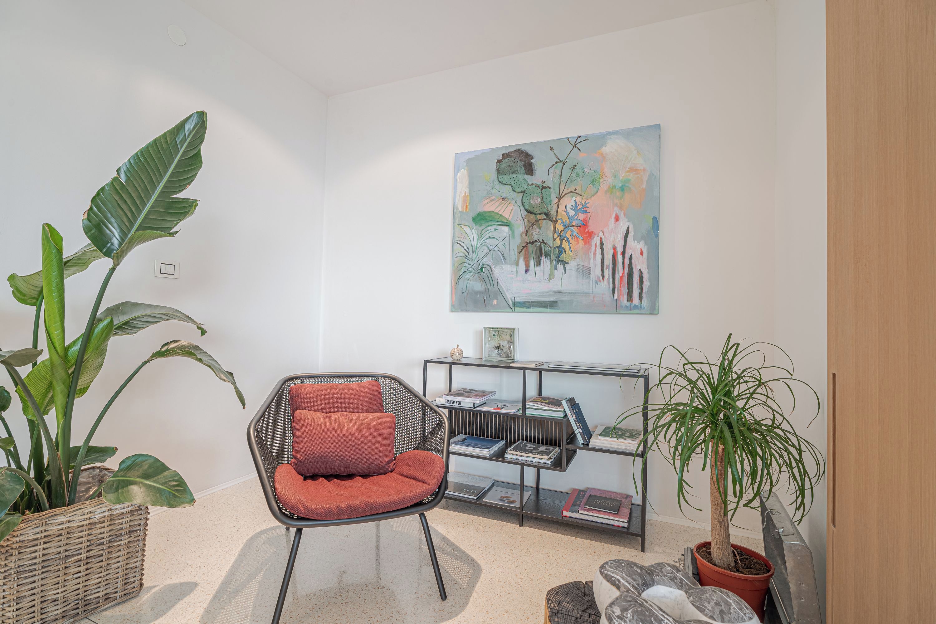 Un soggiorno moderno con una poltrona rossa, una libreria e un grande quadro appeso al muro.