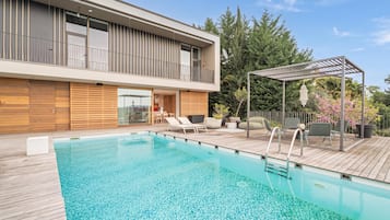 Une maison moderne dotée d’une piscine, d’un espace salon extérieur et d’une pergola.
