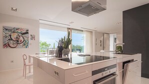 A modern kitchen with a central island, built-in appliances, and a large window offering a view. - Alma Vista Villa in Goriska Brda Pool & Spa (Brda)