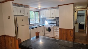 A kitchen with white cabinets, a black countertop, a stove, and a refrigerator.