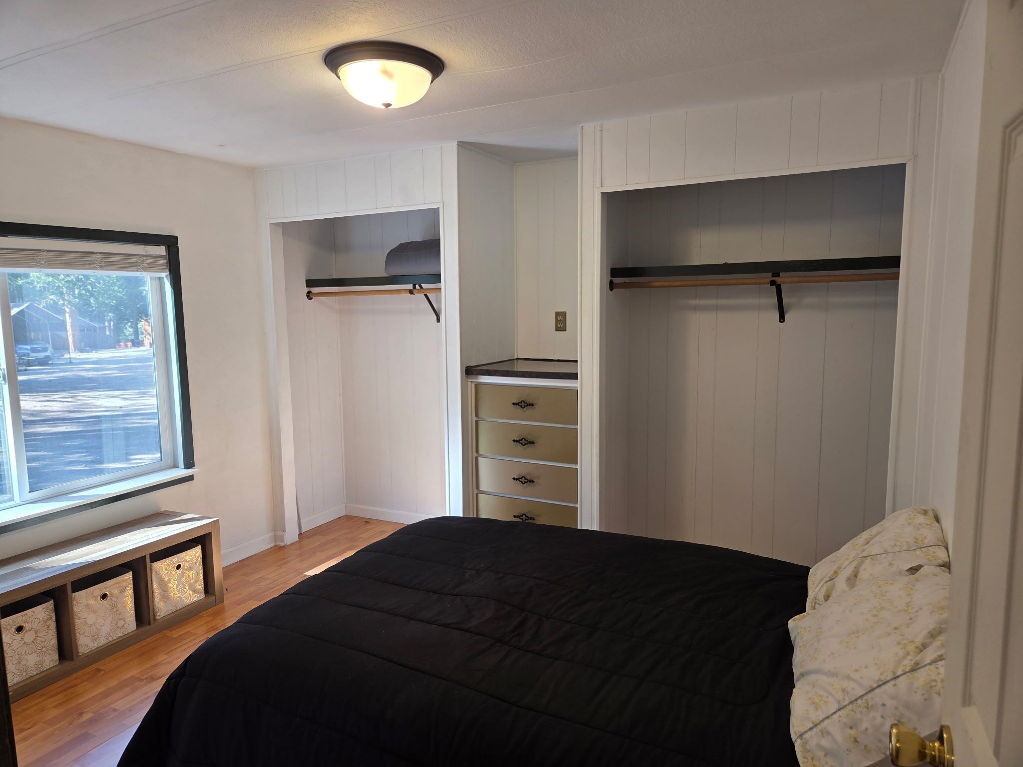 A bedroom with a bed, built-in wardrobe, and a window with a view of the street.