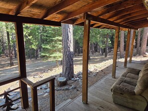 A covered porch with a wooden bench, wooden beams, and a view of a forested area.
