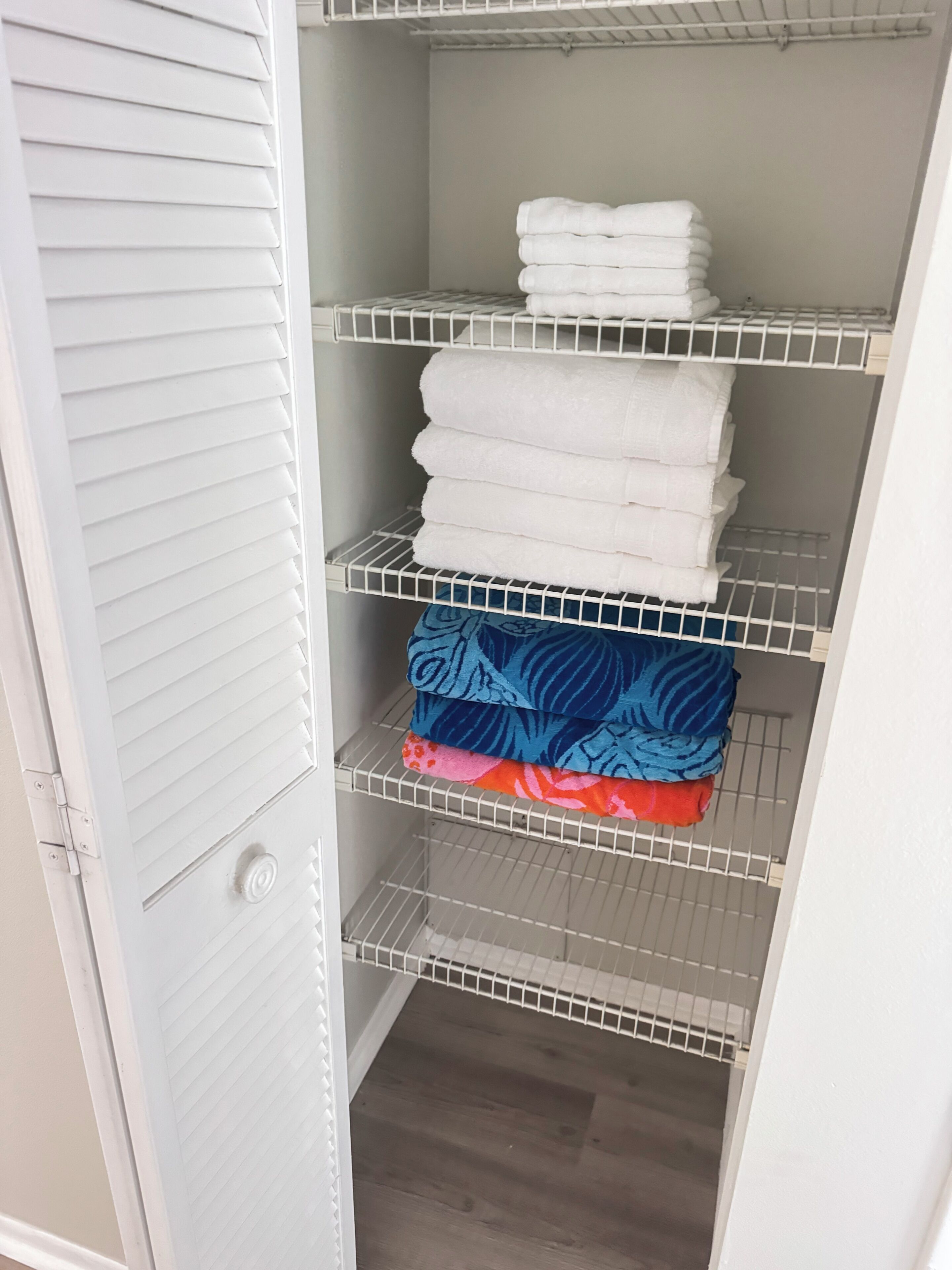 A white closet with three shelves, each holding folded towels and blankets.