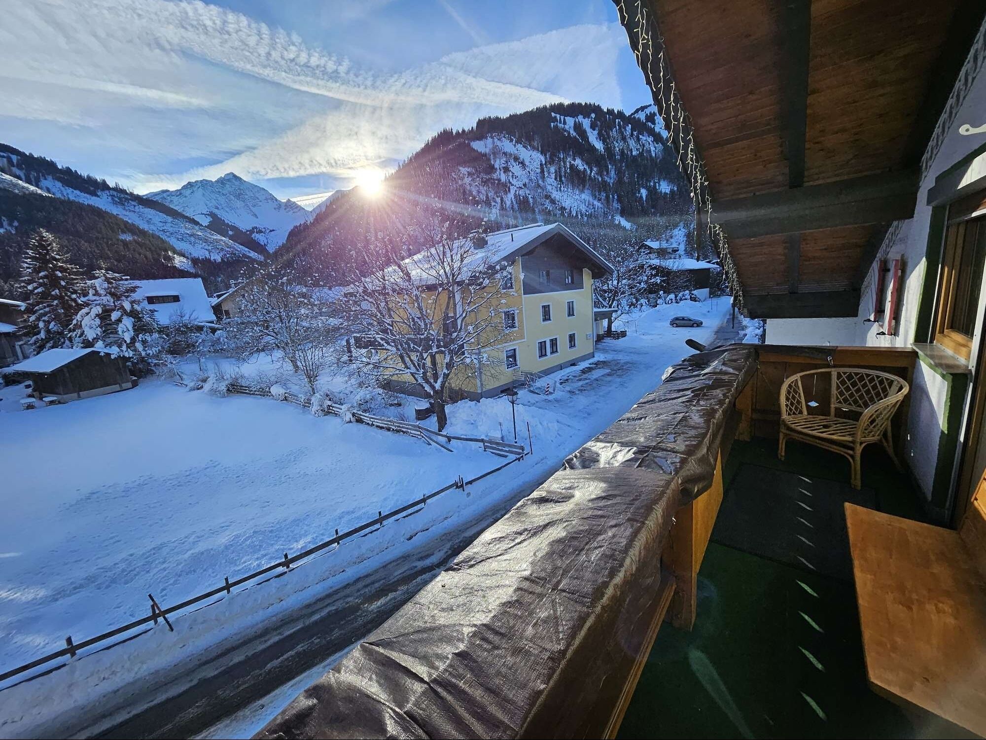 Een besneeuwd berglandschap met een gebouw en een stoel bij een balkon.