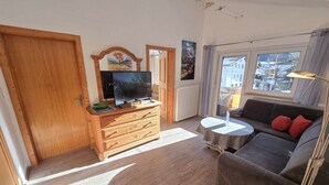 Olohuoneessa on puinen TV-taso, sohva, pieni pöytä ja ikkuna, josta on näkymä rakennuksiin.