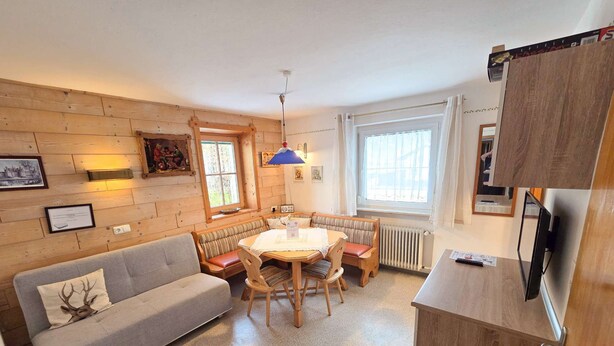 A cozy room with a sofa, a dining table with chairs, a wooden cabinet, and a television. - Ferienwohnungen Luttinger am Mühlbach – Cozy Apartment (Bichlbach)