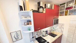 A compact kitchen with a built-in microwave, a coffee maker, and a small shelf with kitchen utensils. - Ferienwohnungen Luttinger am Mühlbach – Cozy Apartment (Bichlbach)
