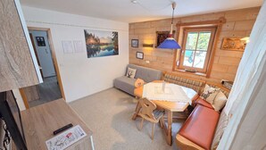 A cozy room with a wooden bench, a table with a lace tablecloth, a sofa, and a window with a view of greenery. - Ferienwohnungen Luttinger am Mühlbach – Cozy Apartment (Bichlbach)