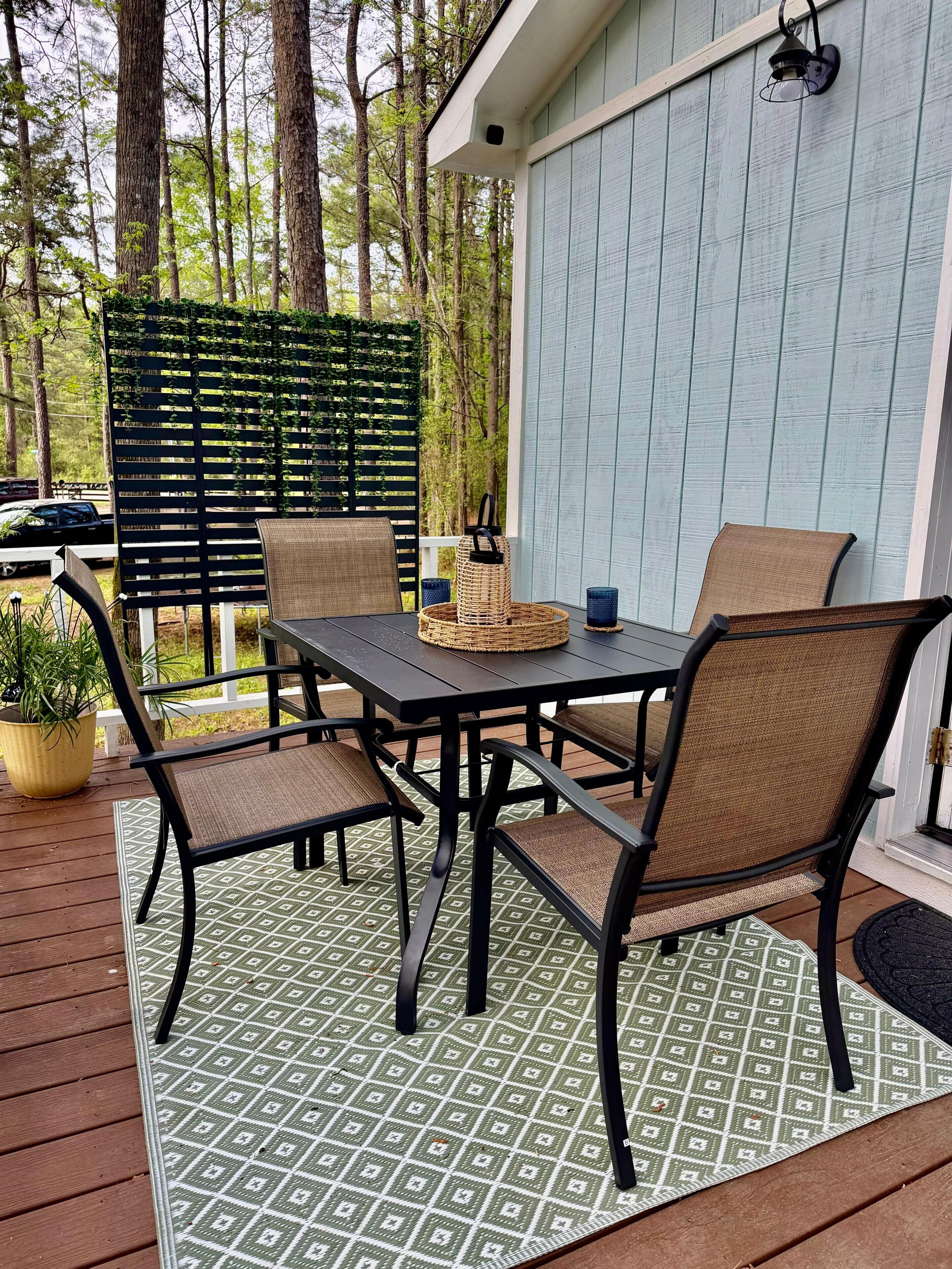 Una terrazza esterna con tavolo e sedie, circondata da un pontile in legno e un tappeto verde decorato.