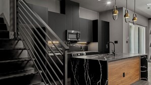 Una cuina moderna amb una illa de marbre, electrodomèstics d'acer inoxidable i una escala negra.