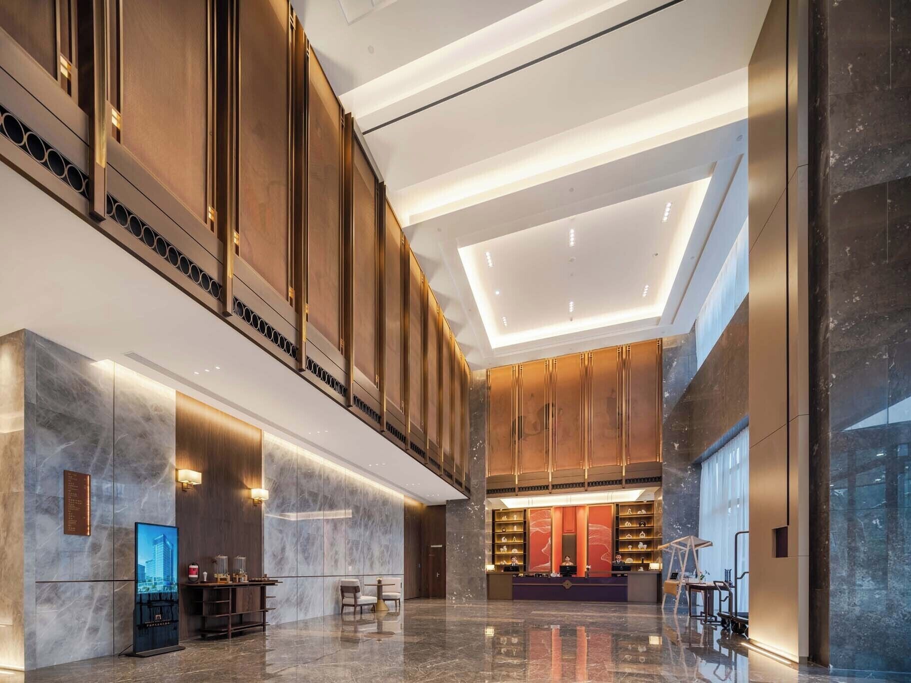 A modern hotel lobby with a reception desk, seating area, and a large display screen.